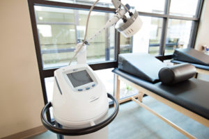 Cascadia of Nampa, Idaho therapy equipment. Therapy treatment machine sits next to a therapy bed with a wedge pillow. The bed is lined up along large windows.