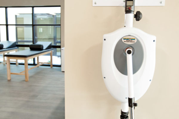 Cascadia of Nampa, Idaho physical therapy equipment. A range of motion machine hangs on the wall. Tall, narrow therapy beds placed along big windows are in the background.
