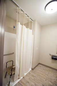 A walk-in shower with a stool and grab bars on the wall.