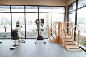 Therapy equipment at Cascadia of Nampa, Idaho. Recumbent bikes, a treadmill and stepping platform are lined up facing large windows in a therapy room.