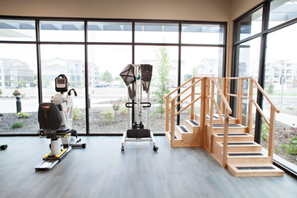 Therapy equipment at Cascadia of Nampa, Idaho. Recumbent bikes, a treadmill and stepping platform are lined up facing large windows in a therapy room.