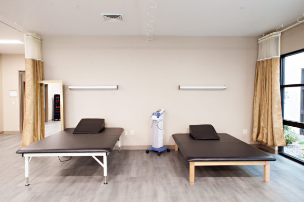Cascadia of Nampa, Idaho physical therapy and rehabilitation area. Two low, wide therapy tables are placed against a wall with lights above each bed.